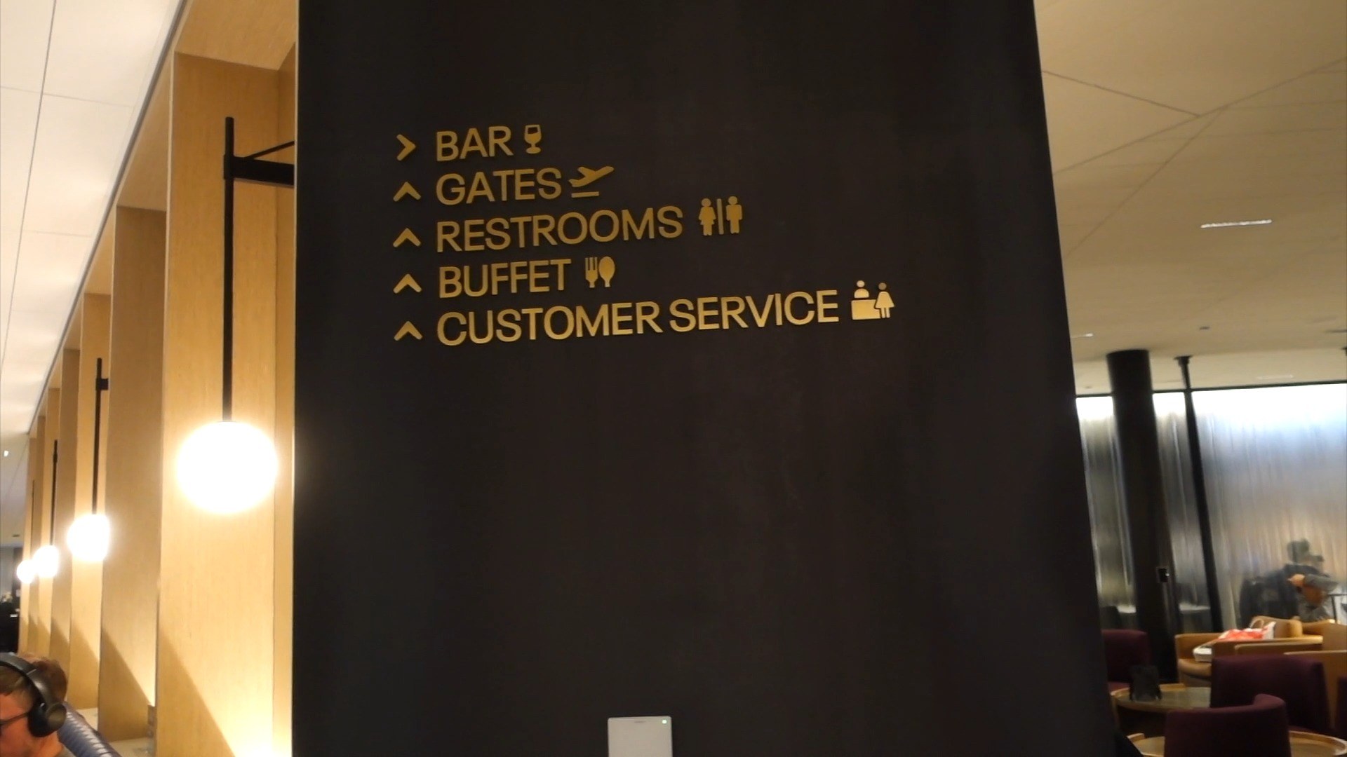 Gold-on-black wayfinding sign at the United Club at ORD Concourse C pointing to bar, gates, restrooms, buffet, and customer service.