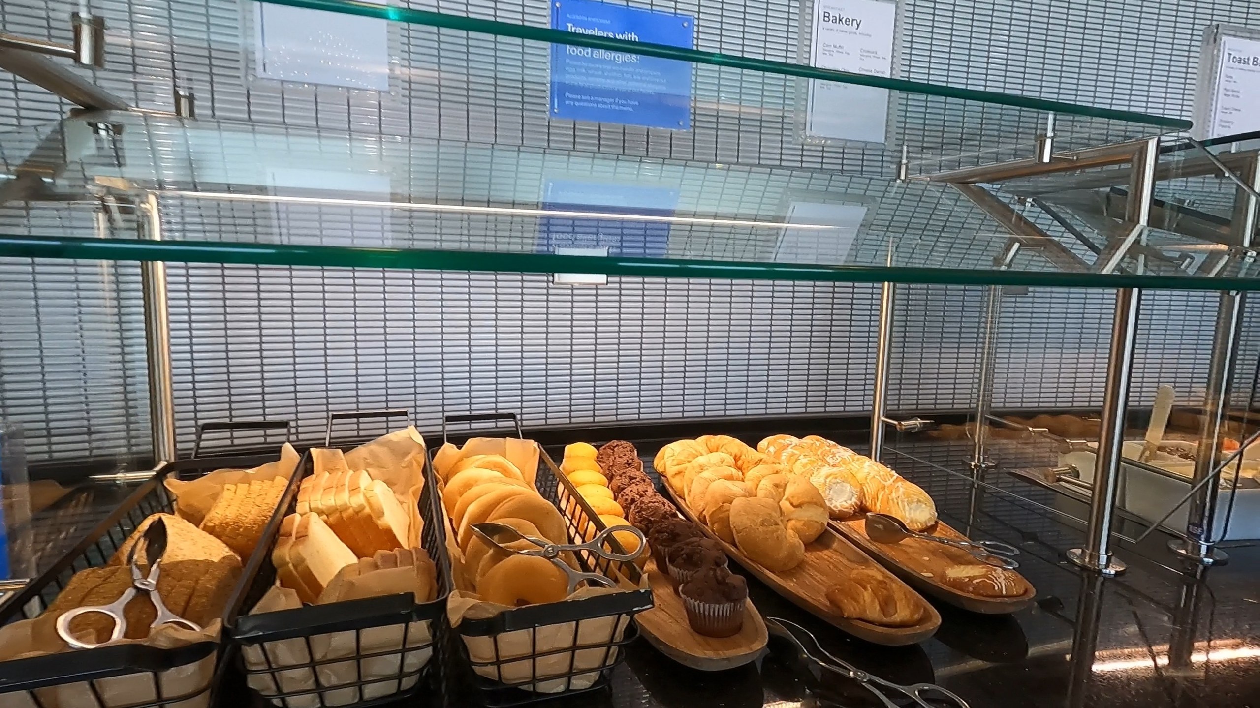 Bakery counter at the United Club at ORD Concourse F with baskets of sliced sandwich bread, brioche rolls, dinner rolls, and chocolate muffins.