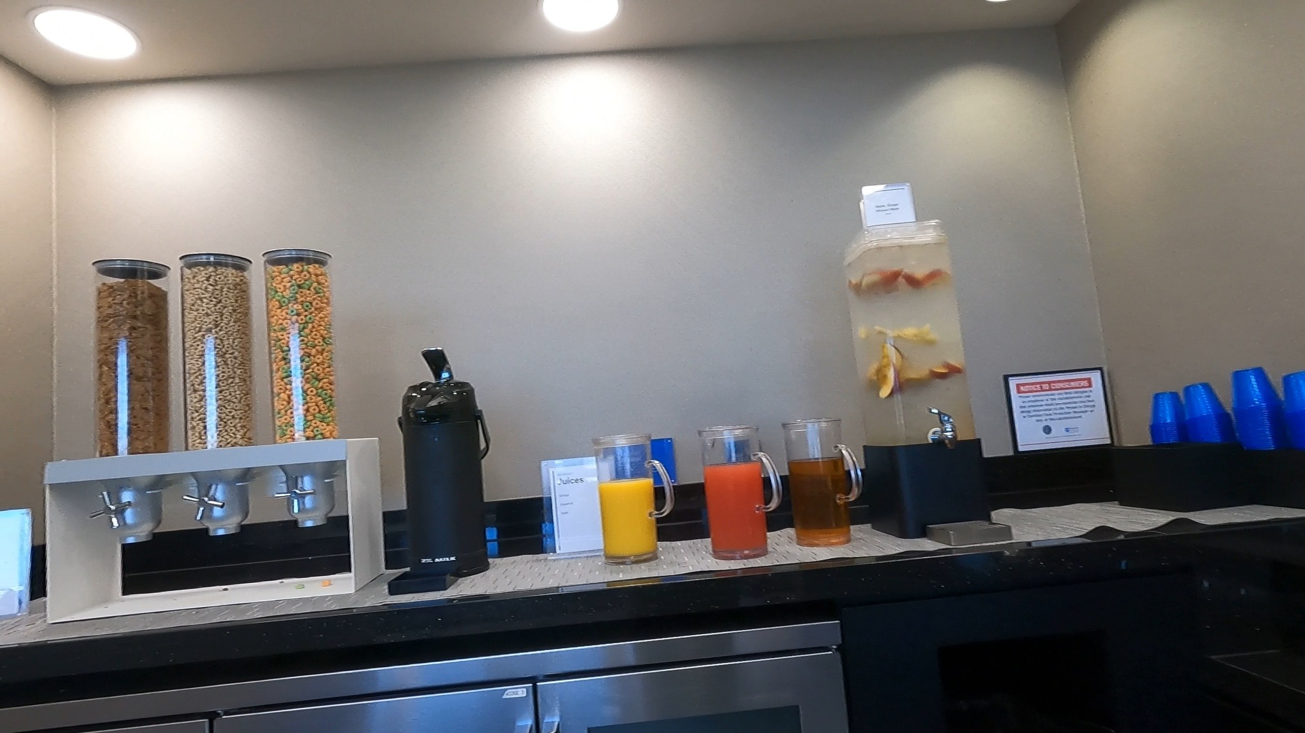 Breakfast drinks station at the United Club at ORD Concourse F with three cereal dispensers, a coffee thermos, juice pitchers, and a fruit-infused water dispenser.