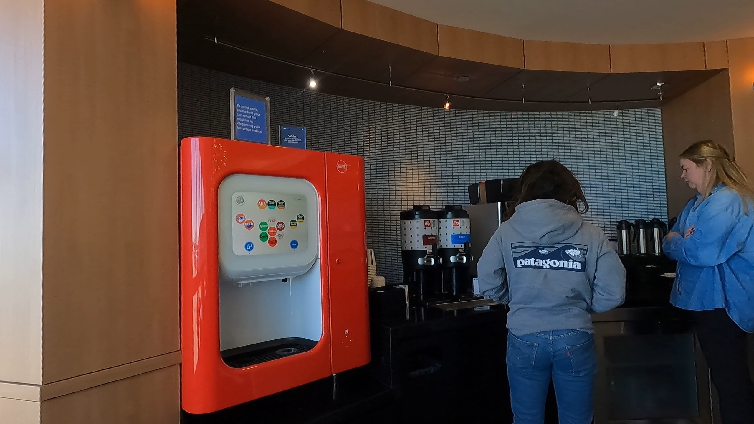 Coca-Cola Freestyle and twin coffee dispensers at the United Club at ORD Concourse F under a curved wood-paneled wall.