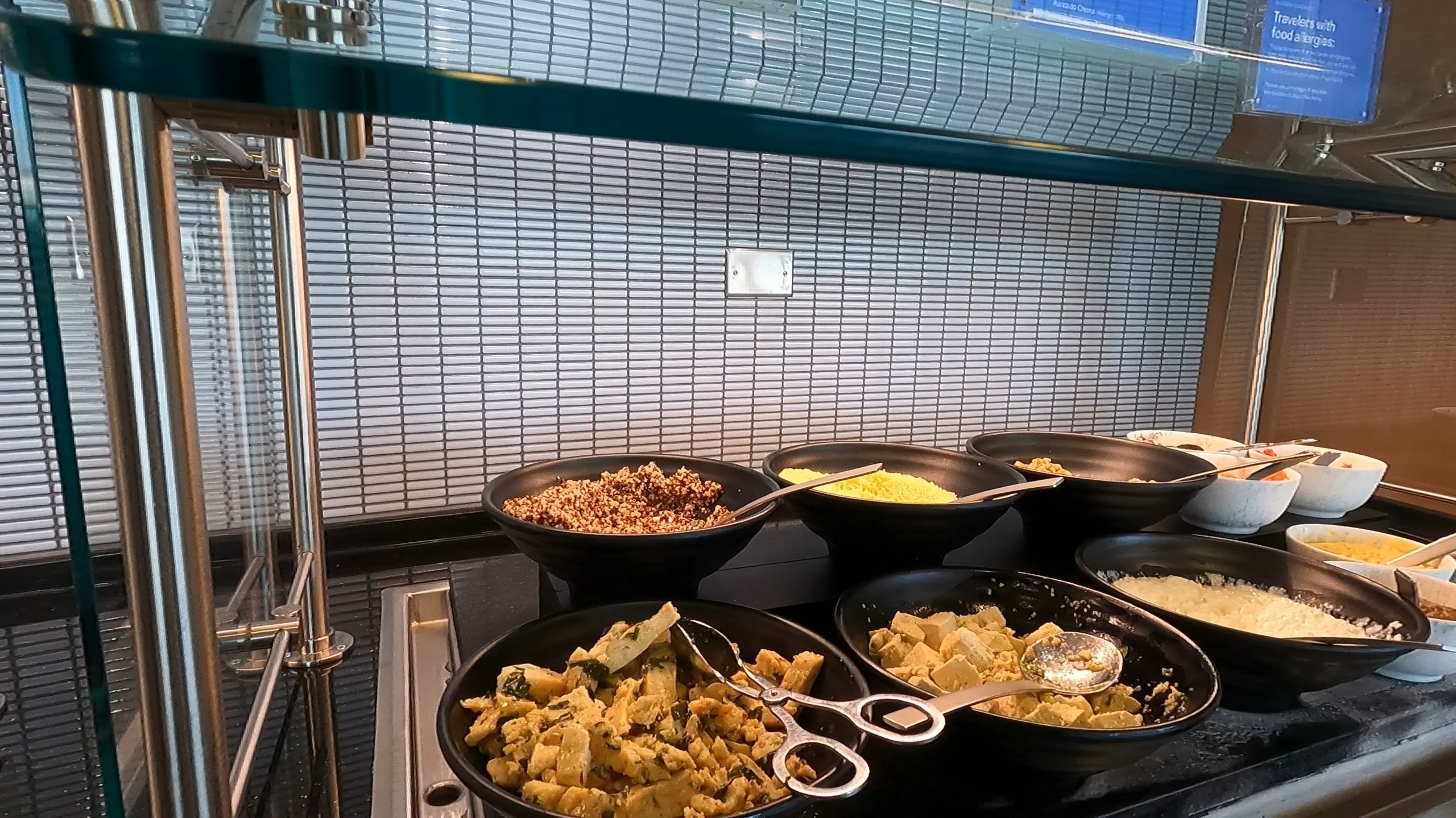 Hot breakfast spread at the United Club at ORD Concourse F with quinoa, scrambled eggs, sausage, oatmeal, and other warm dishes in serving pans.