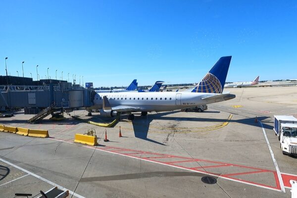 Tarmac view from the United Club at ORD Concourse F with a United Express Embraer E175 regional jet at the gate and a clear blue sky overhead.
