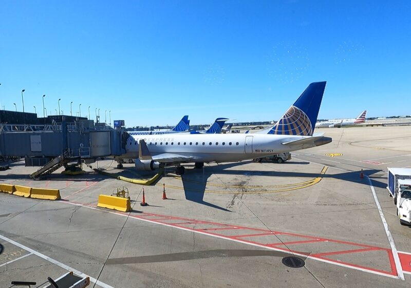 Tarmac view from the United Club at ORD Concourse F with a United Express Embraer E175 regional jet at the gate and a clear blue sky overhead.