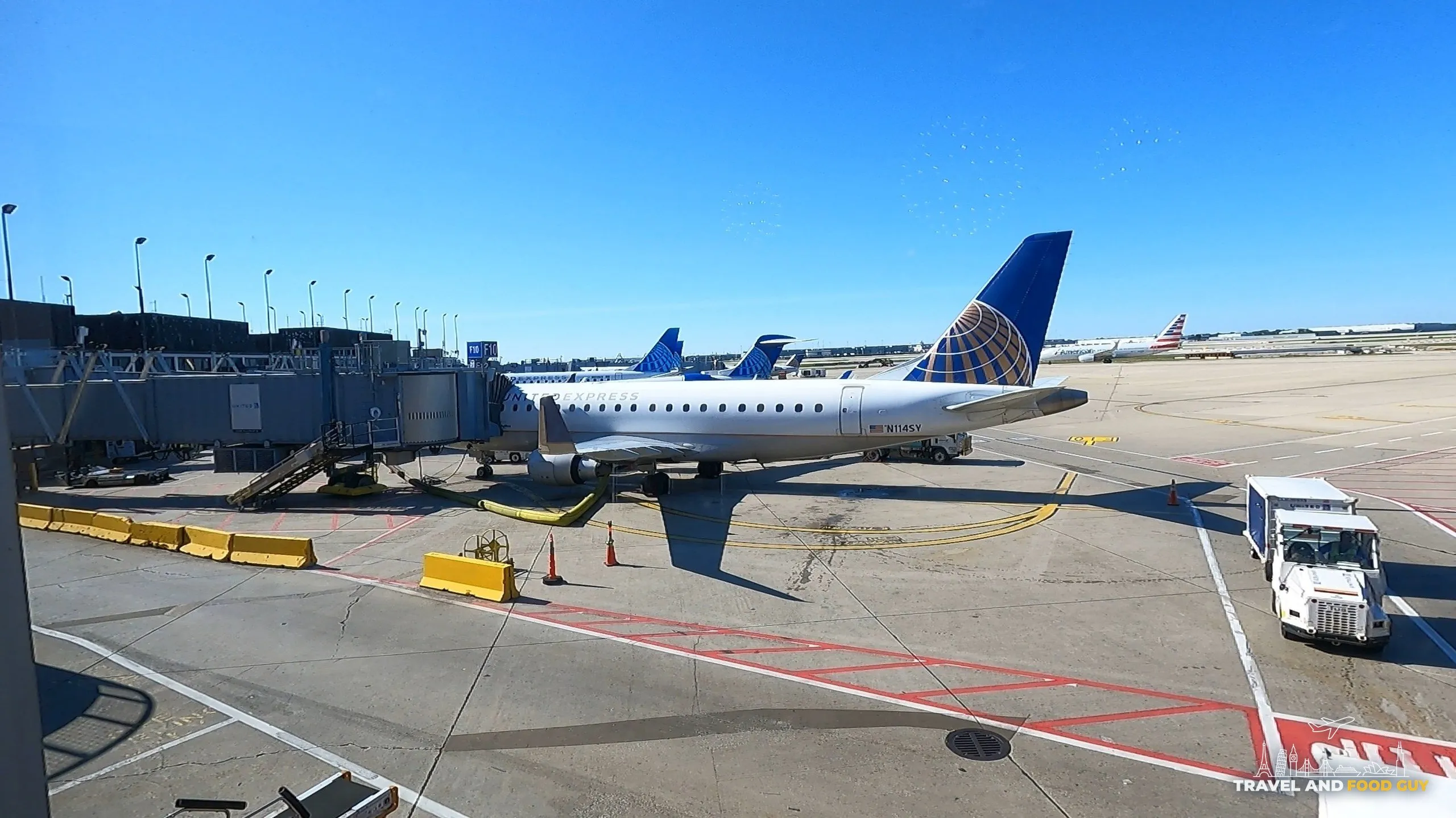 Tarmac view from the United Club at ORD Concourse F with a United Express Embraer E175 regional jet at the gate and a clear blue sky overhead.