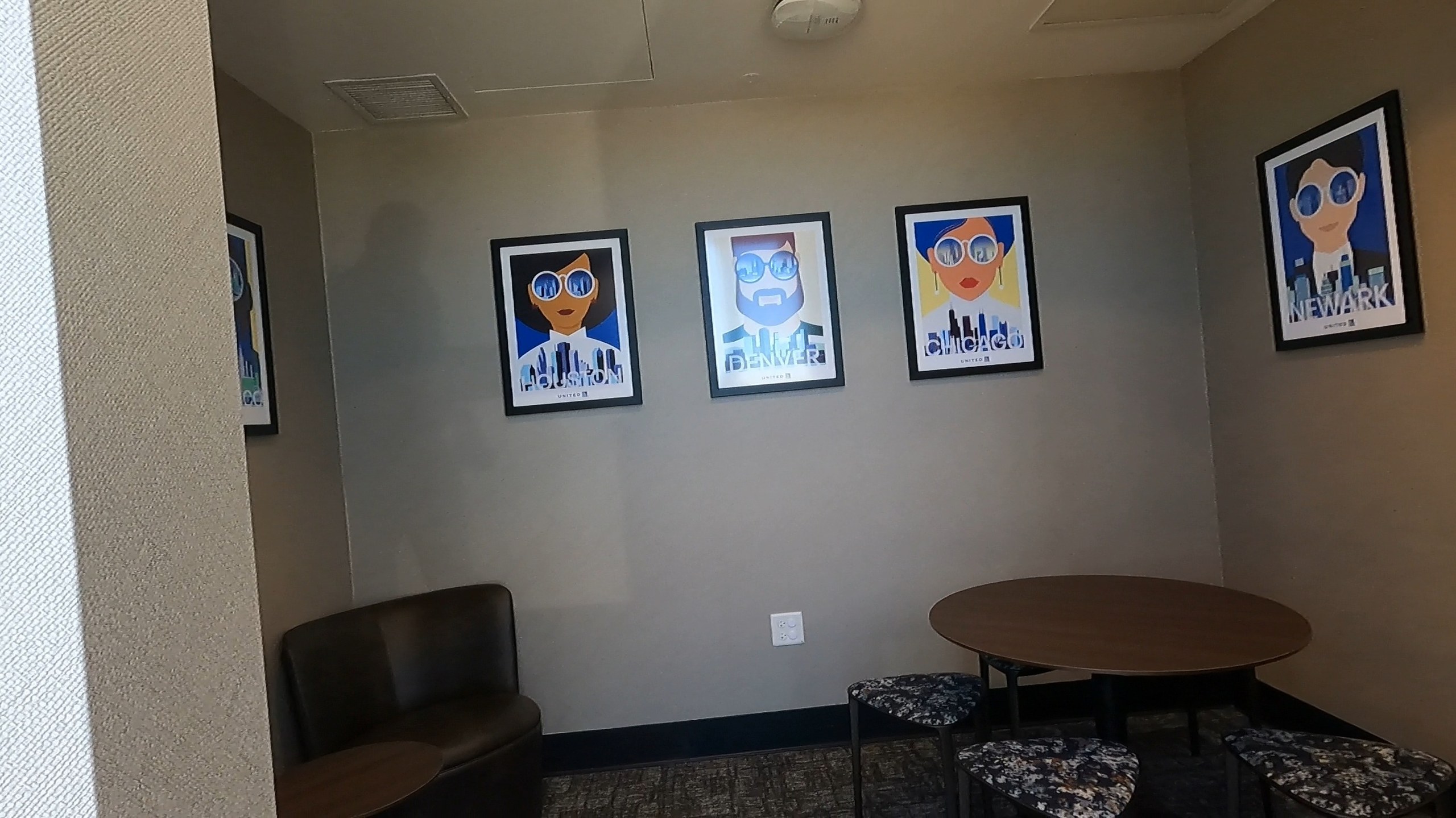 Wall of United city posters (Houston, Denver, Chicago, Newark) above a small lounge area at the United Club at ORD Concourse F.