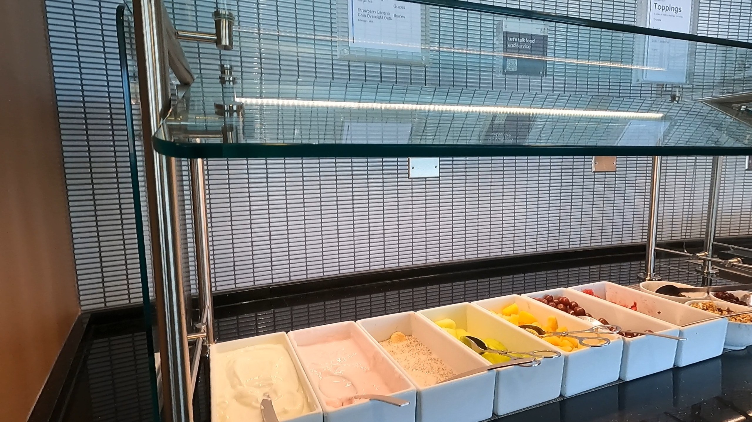 Yogurt and fruit bar at the United Club at ORD Concourse F with cottage cheese, granola, melon, oranges, dried cranberries, and other toppings in white serving dishes.