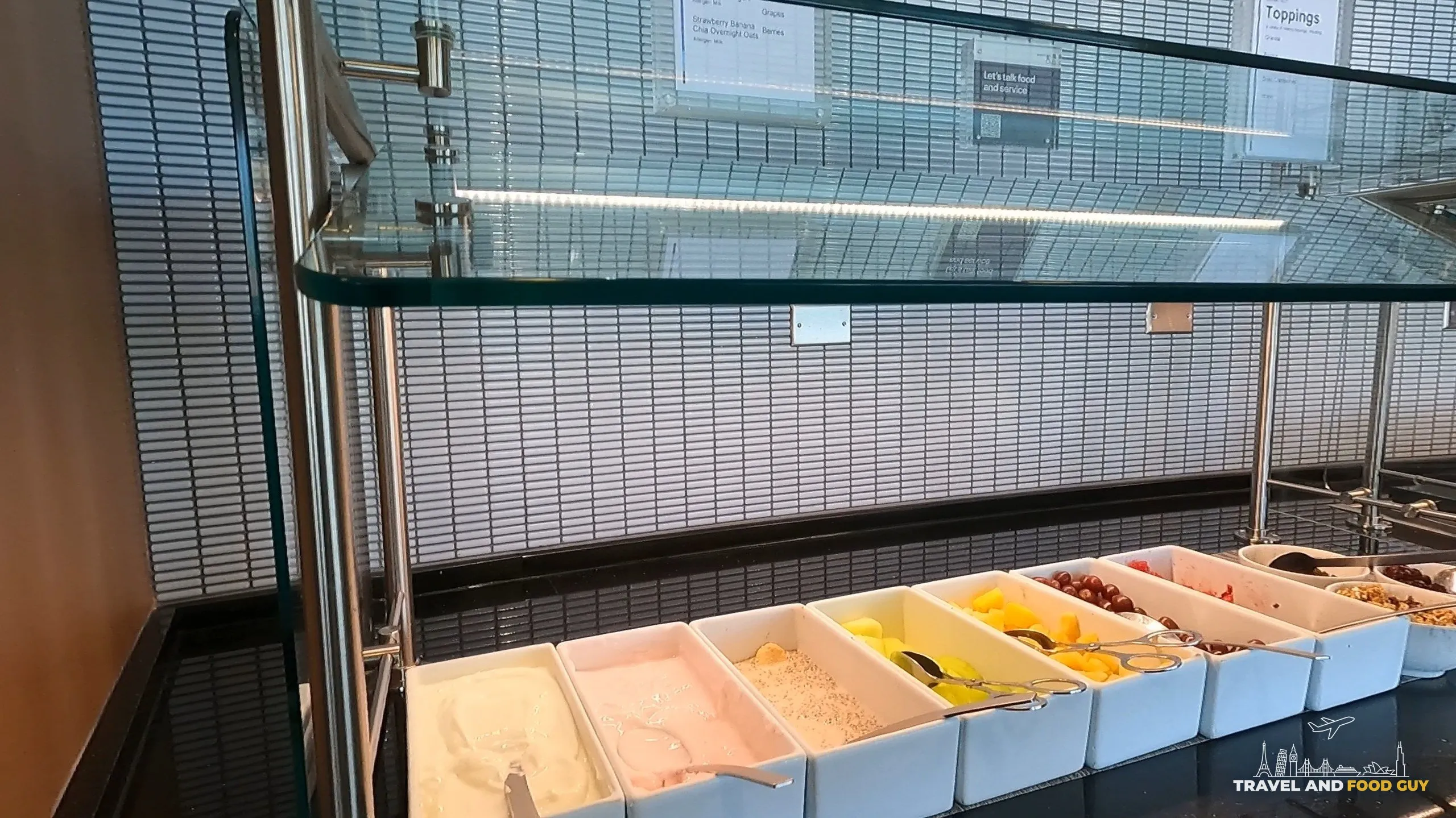 Yogurt and fruit bar at the United Club at ORD Concourse F with cottage cheese, granola, melon, oranges, dried cranberries, and other toppings in white serving dishes.