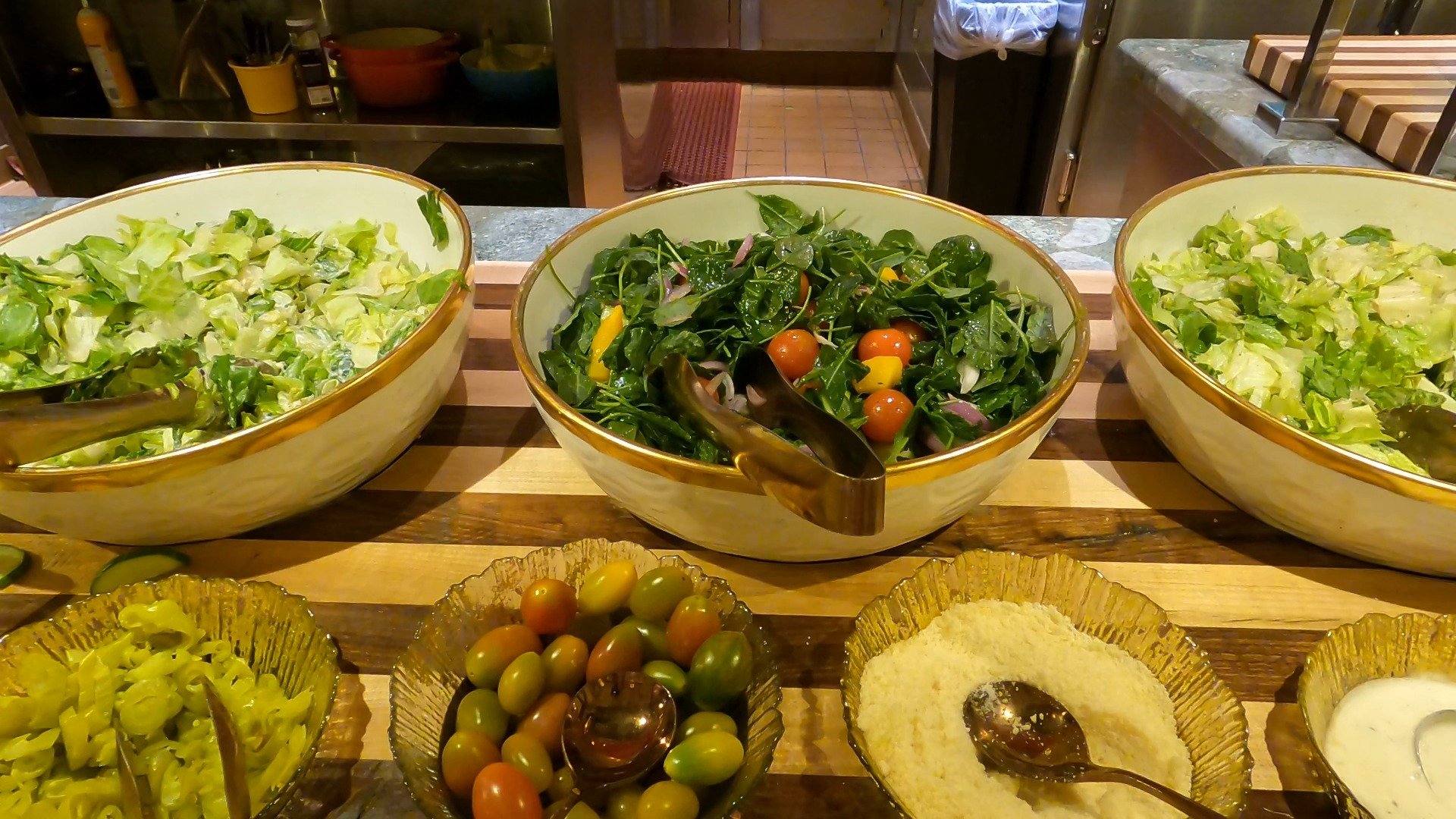 Salad station at The Buffet at Wynn with three large bowls of greens and small bowls of pickles, tomatoes, and parmesan