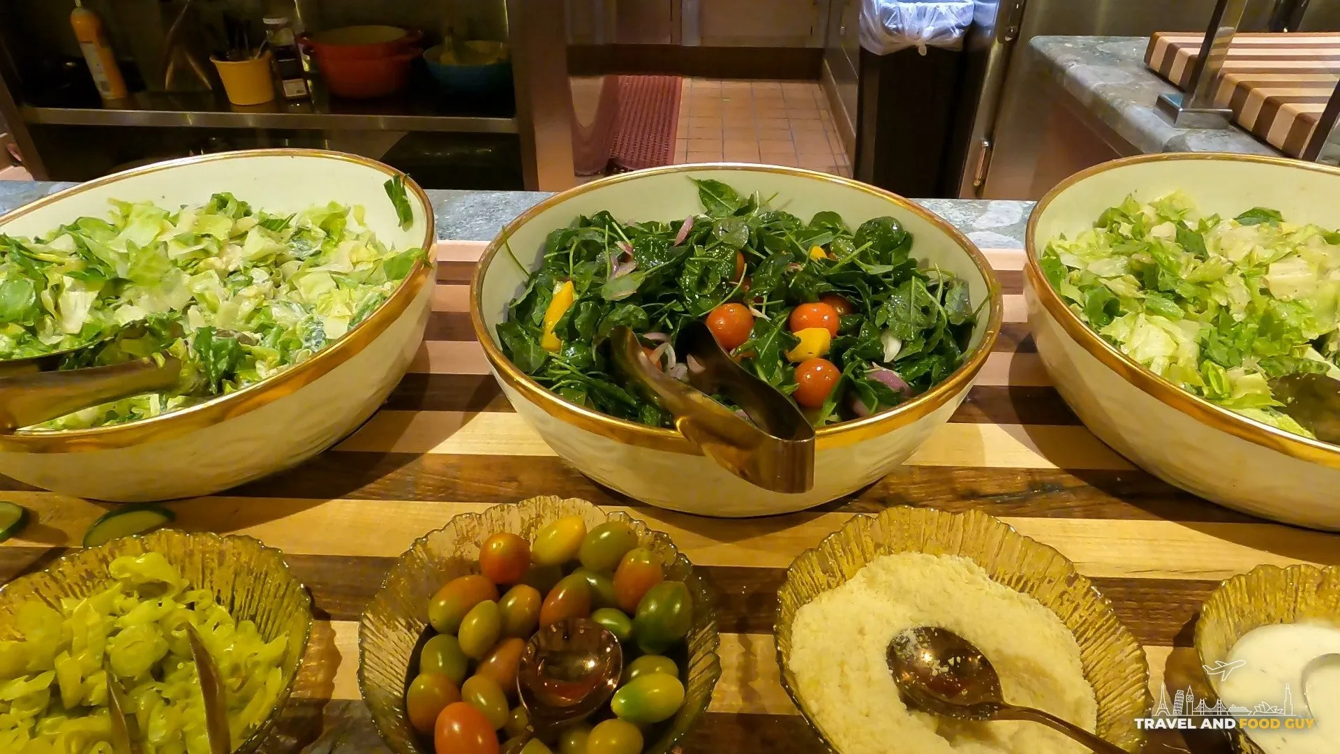 Salad station at The Buffet at Wynn with three large bowls of greens and small bowls of pickles, tomatoes, and parmesan