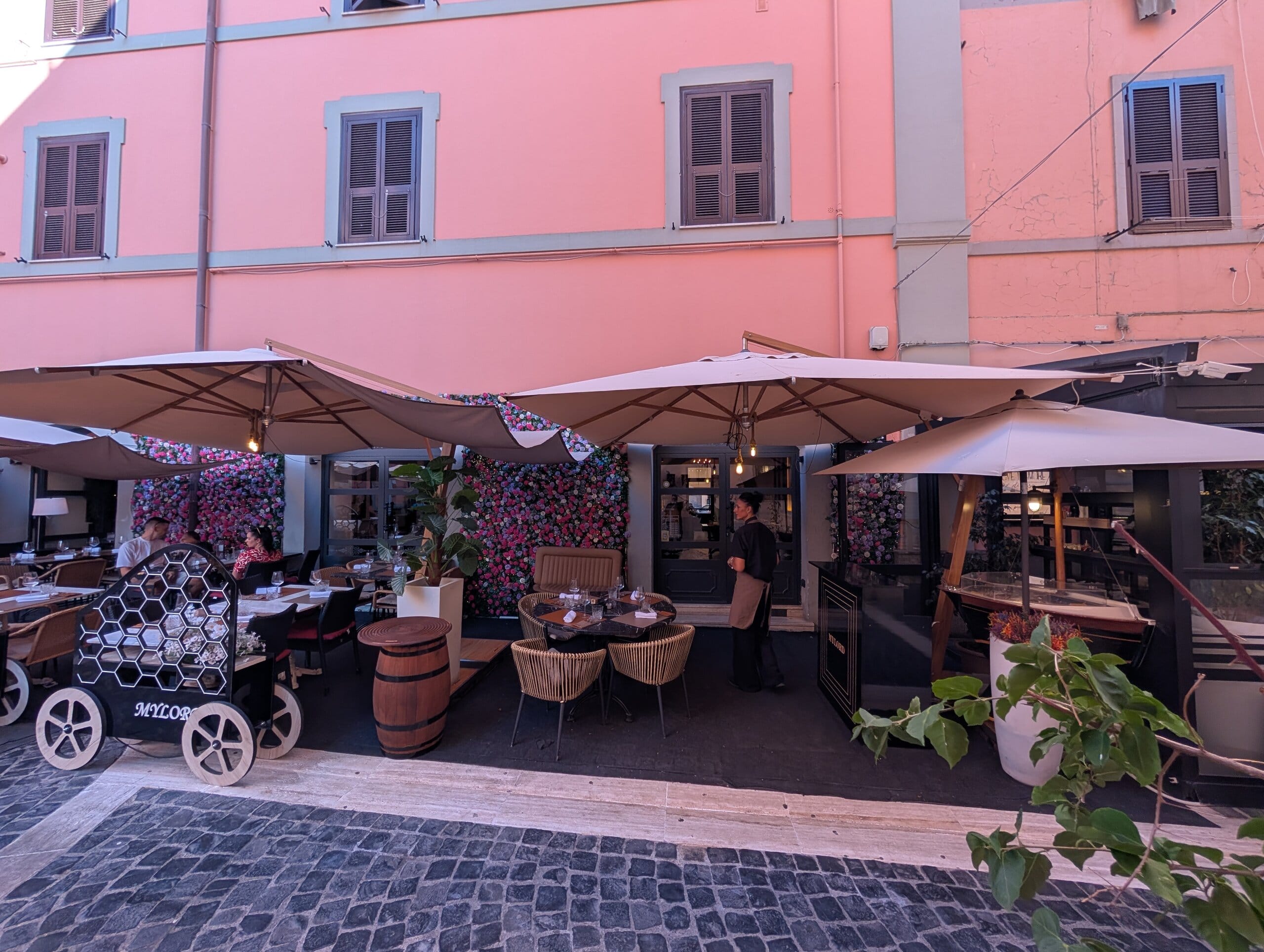 Outdoor terrace at Mylord in Civitavecchia with umbrellas and flower walls on a cobblestone lane
