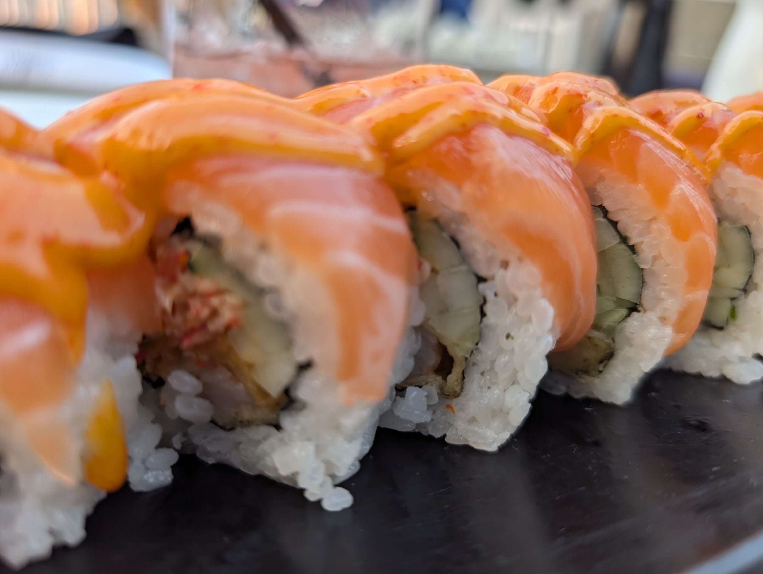 Close up of the Hikaru roll at Shakou showing shrimp tempura, spicy crab and cucumber under fresh salmon