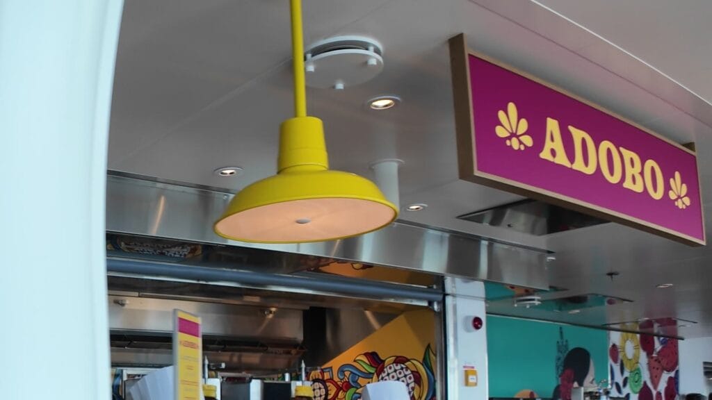 The pink Adobo stand sign, complete with its flower marks, above the al pastor taco counter in the AquaDome Market on Legend of the Seas.