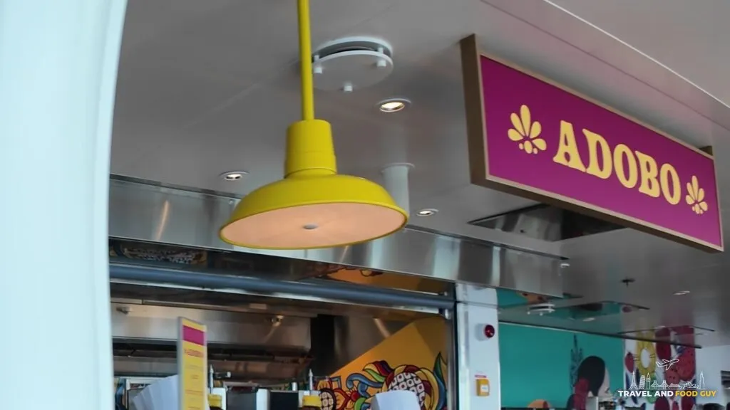 The pink Adobo stand sign, complete with its flower marks, above the al pastor taco counter in the AquaDome Market on Legend of the Seas.