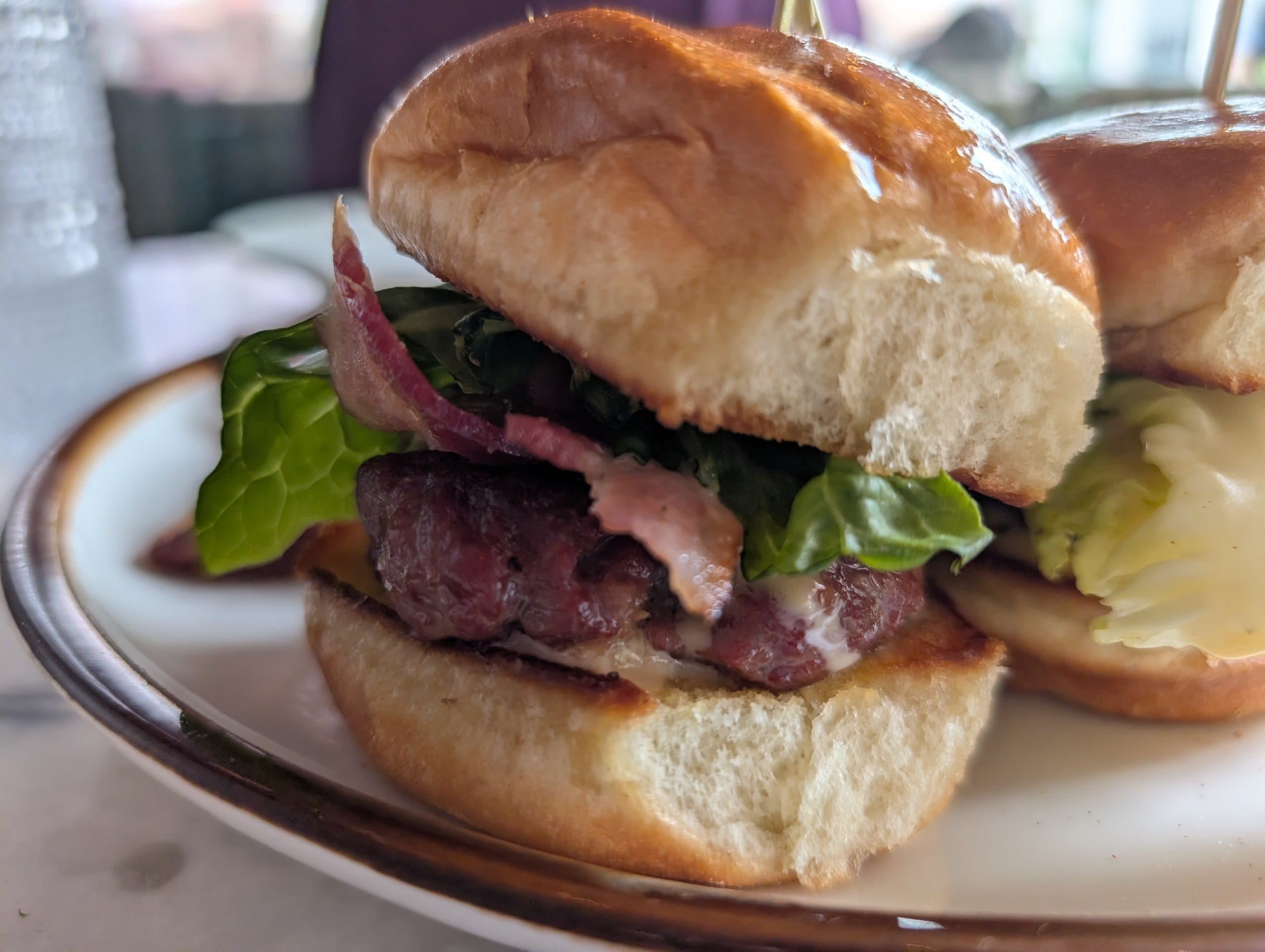 A close look at one Ambar slider, smoked gouda melting over the beef with bacon, pickled red onion and lettuce on a brioche bun.