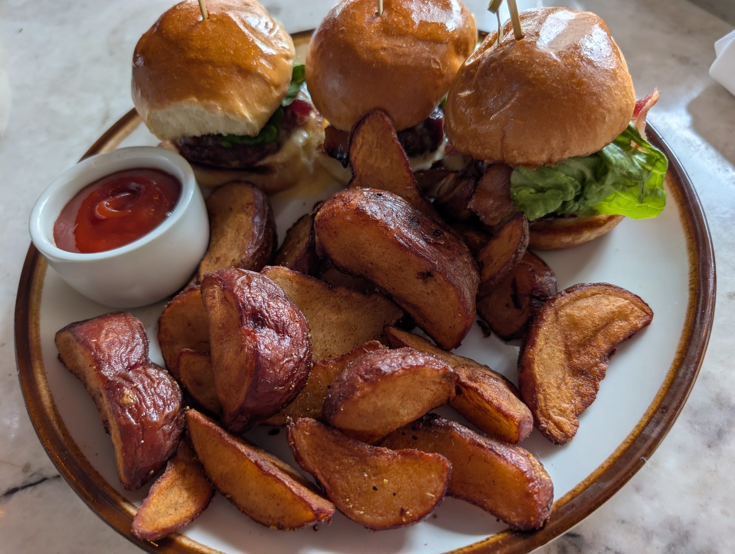 Three Ambar sliders arrive on brioche with a pile of crisp roasted breakfast potatoes and a ramekin of ketchup.