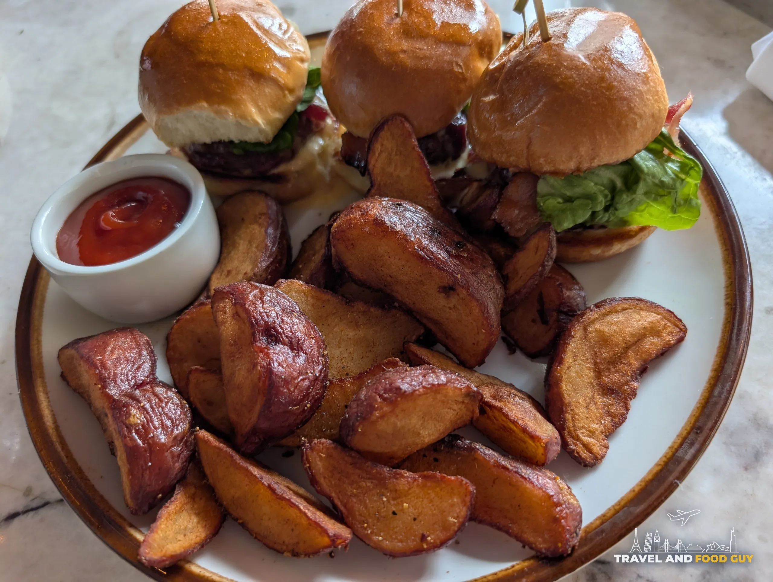 Three Ambar sliders arrive on brioche with a pile of crisp roasted breakfast potatoes and a ramekin of ketchup.