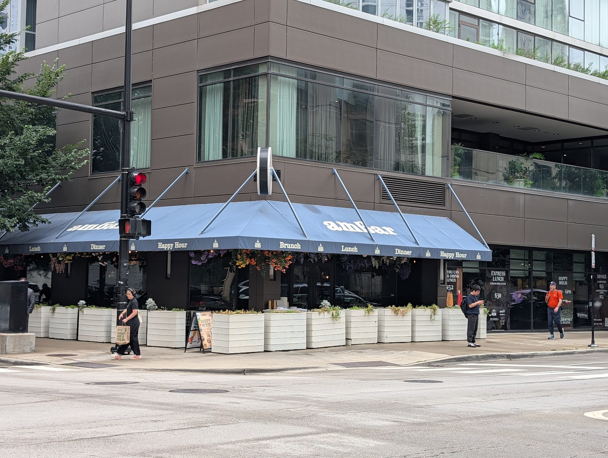 The wraparound blue awning lists lunch, dinner, brunch and happy hour, with the unlimited pricing board mounted beside the entrance.
