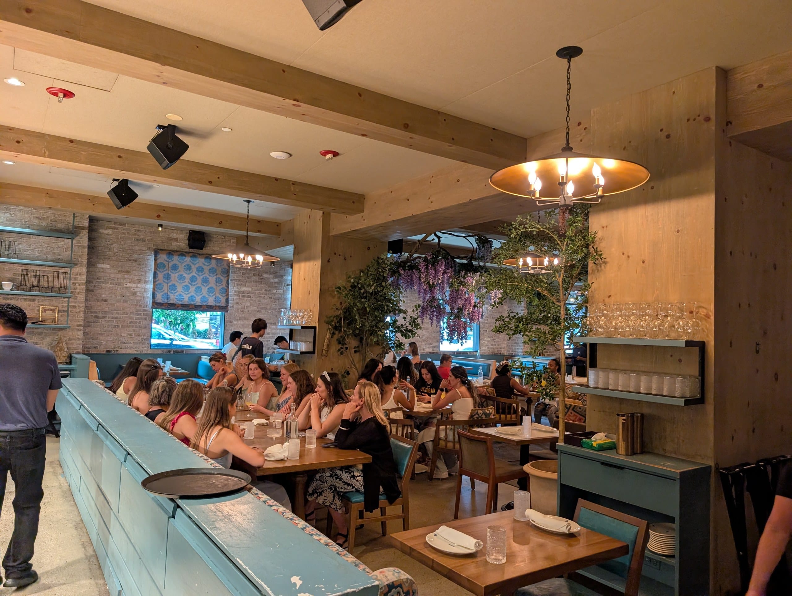 A long blue service bar runs beside the back dining room, where a large party fills the communal tables under exposed brick and beams.