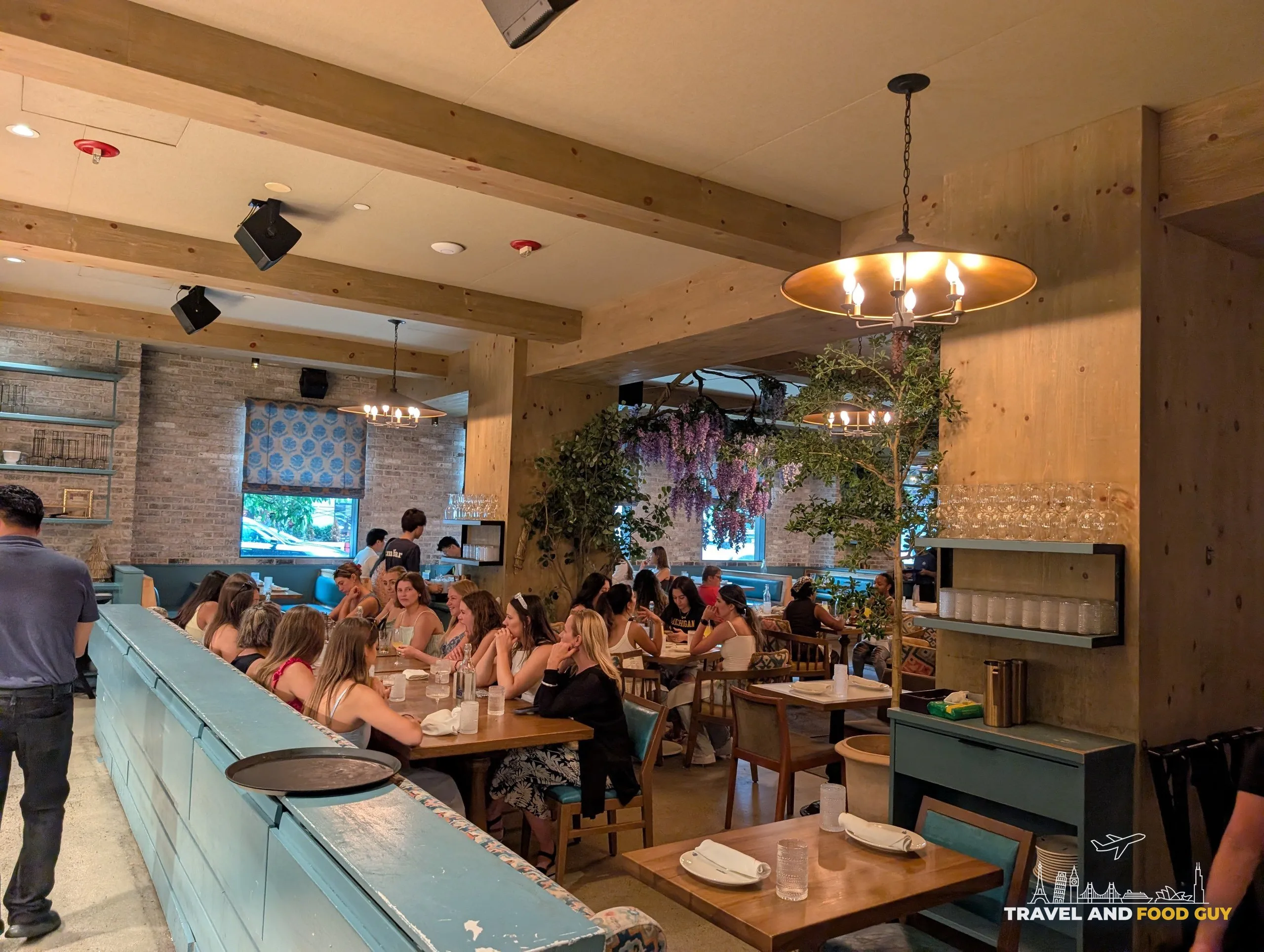 A long blue service bar runs beside the back dining room, where a large party fills the communal tables under exposed brick and beams.