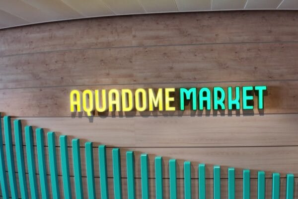 The AquaDome Market wall sign on deck 15 of Legend of the Seas, gold and teal three dimensional lettering on a wood wall above the teal fin sculpture.