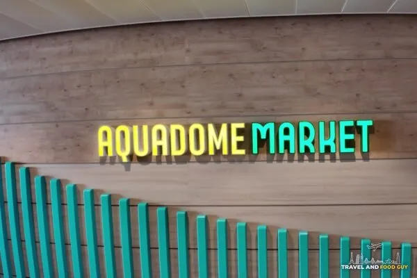 The AquaDome Market wall sign on deck 15 of Legend of the Seas, gold and teal three dimensional lettering on a wood wall above the teal fin sculpture.