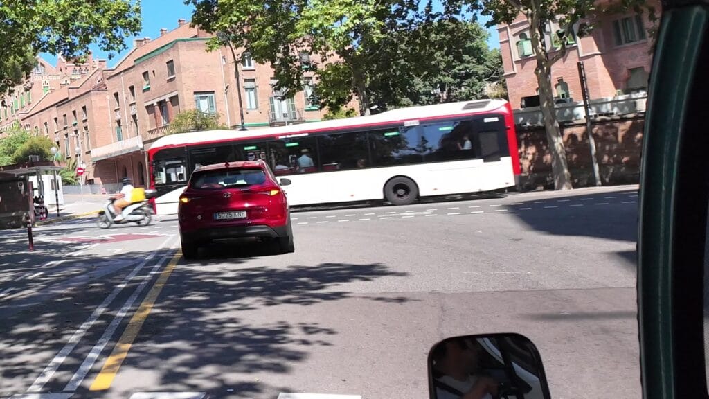 A red and white TMB city bus crossing an intersection in Barcelona on a bright summer afternoon