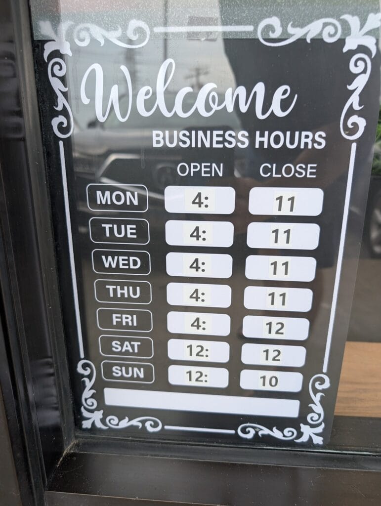 The hours board at the entrance: four in the afternoon Monday through Friday, noon on Saturday and Sunday.