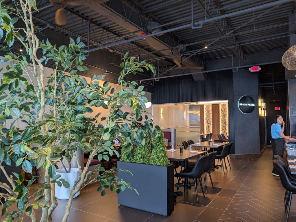 Planted trees divide the main room, with the lit Black Pearl logo and the private room beyond.