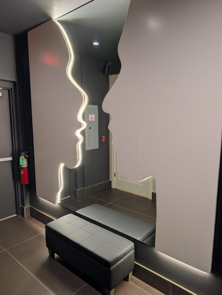 A backlit wavy mirror and bench in the restroom vestibule.