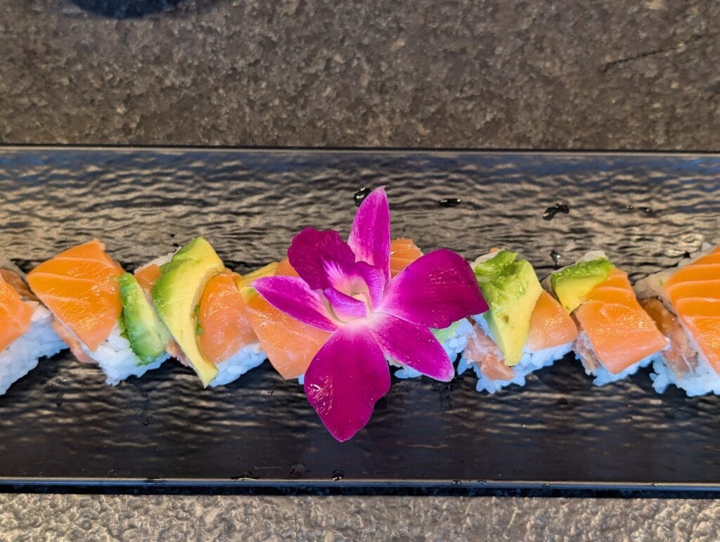 Salmon and avocado over spicy salmon on the Sake Aisiteru roll, finished with an orchid.