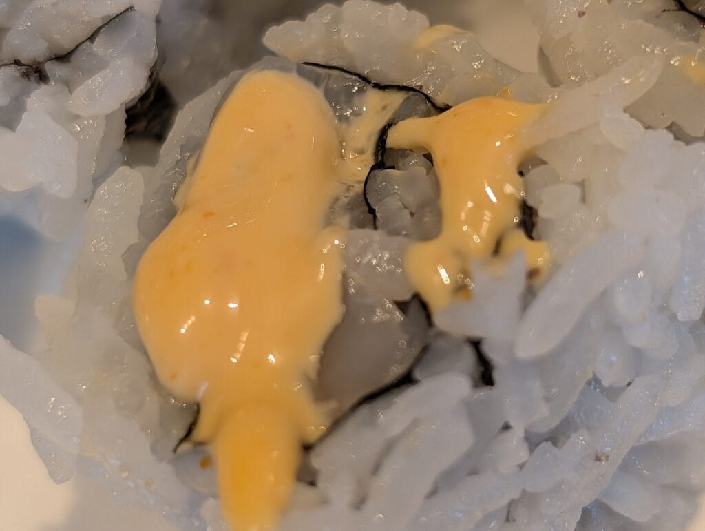 A close look at the spicy mayo on the scallop roll, thin and pale with visible flecks.