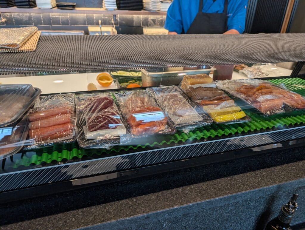 The refrigerated case along the sushi counter, with the fish portioned and held behind glass.
