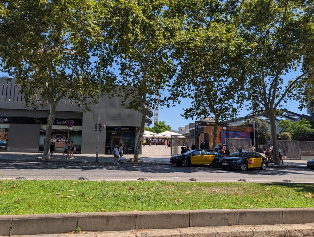 Two complete black and yellow Barcelona taxis waiting at a taxi rank on the tree lined street outside the Camp Nou stadium entrance