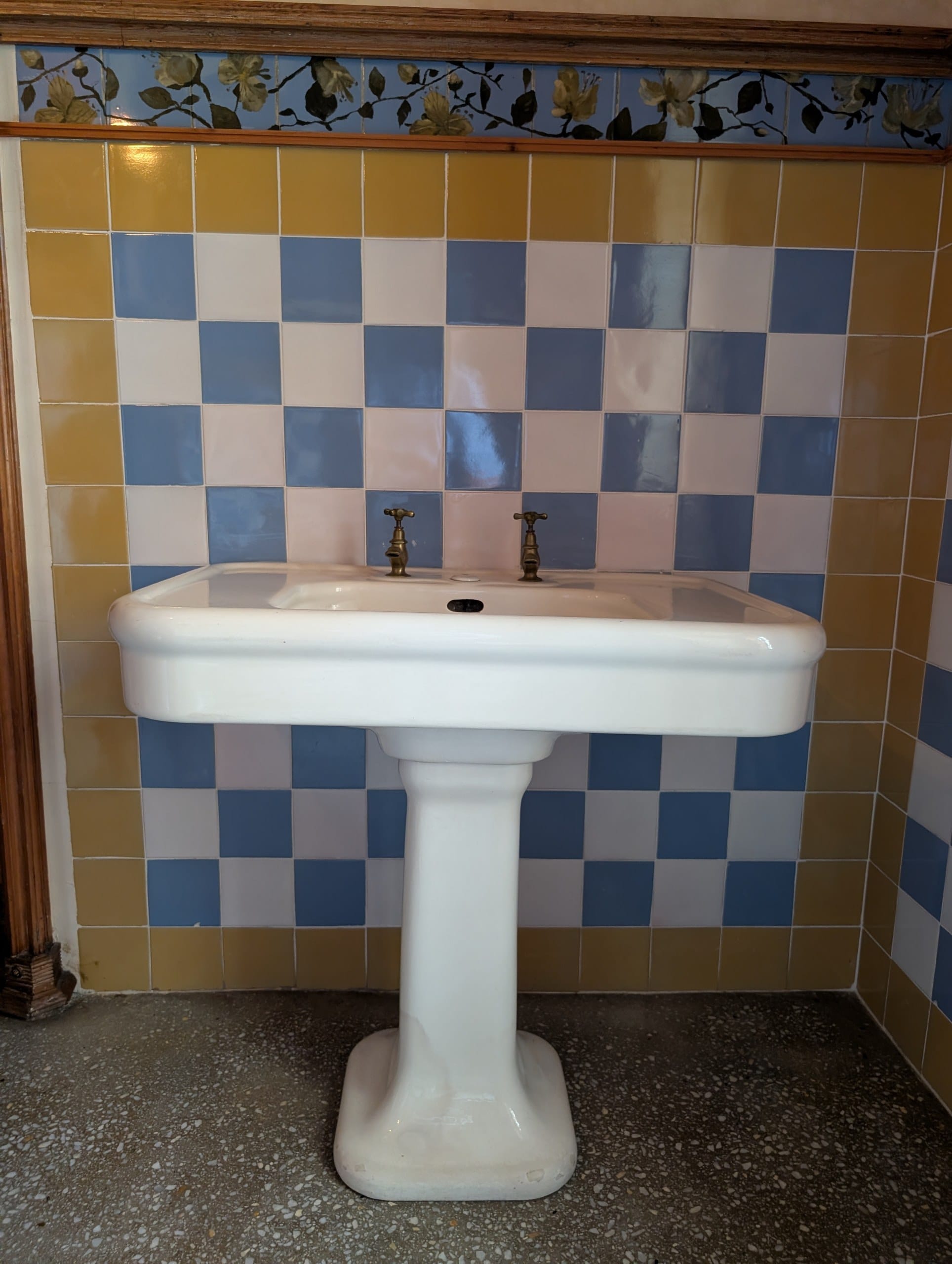 Original pedestal sink and brass taps against checkerboard tile at Casa Vicens