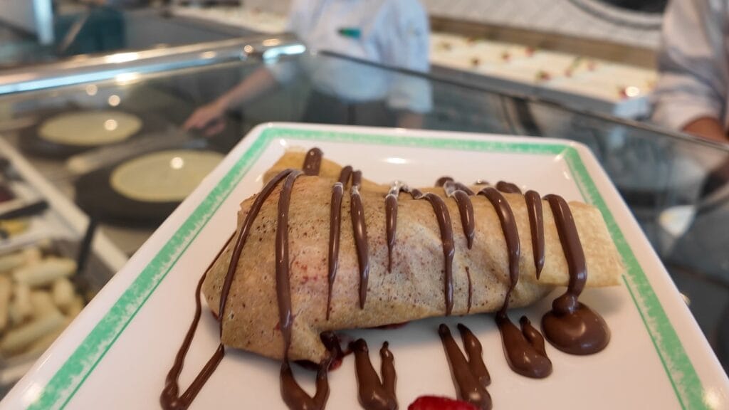 A banana and chocolate crepe made to order at Creme de la Crepe, folded on a plate under a chocolate drizzle.