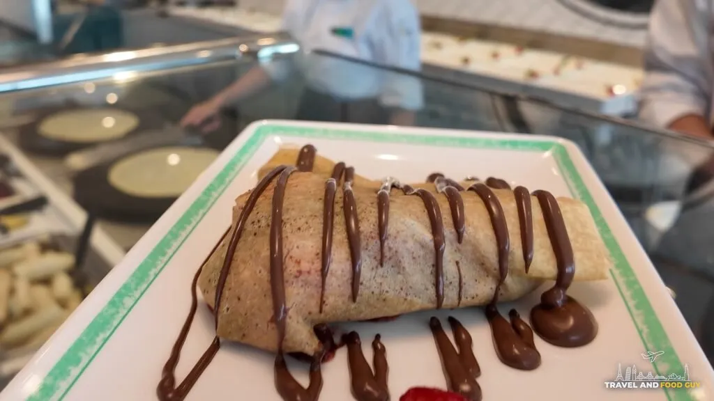 A banana and chocolate crepe made to order at Creme de la Crepe, folded on a plate under a chocolate drizzle.