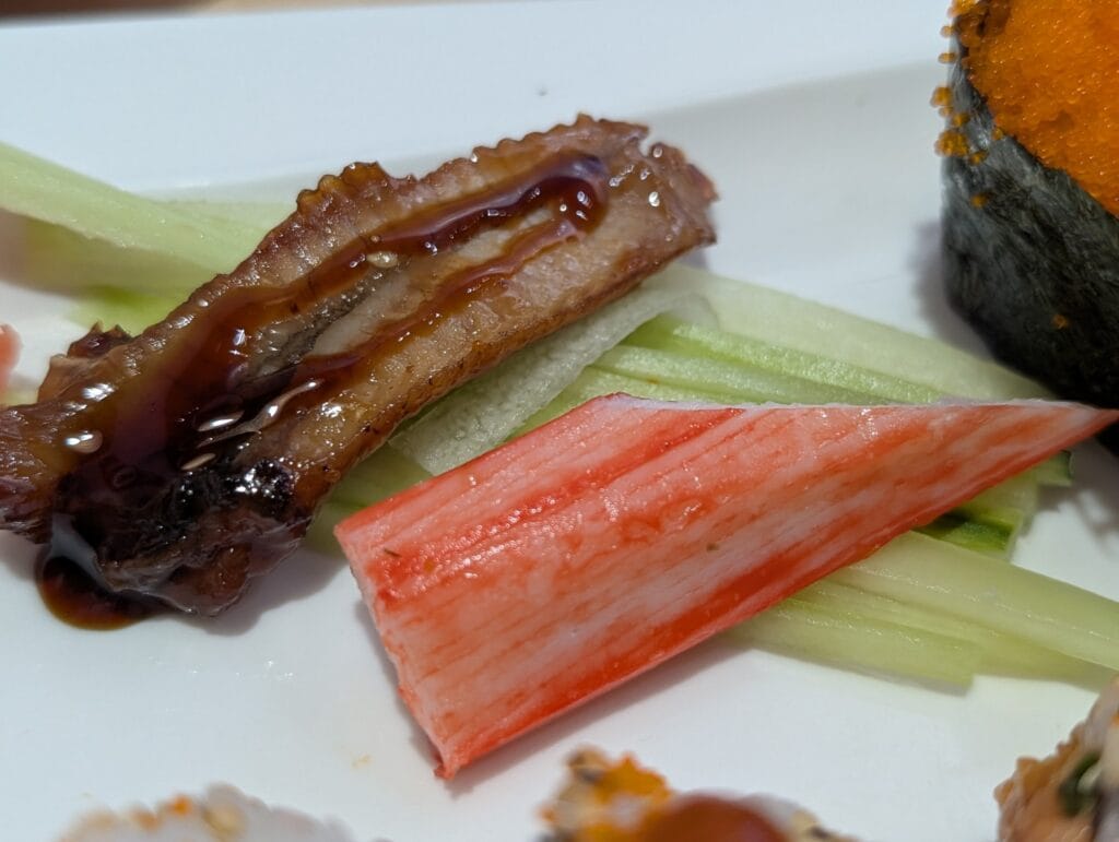 Glazed eel with sesame and a wedge of crab stick over julienned cucumber at e Sushi.