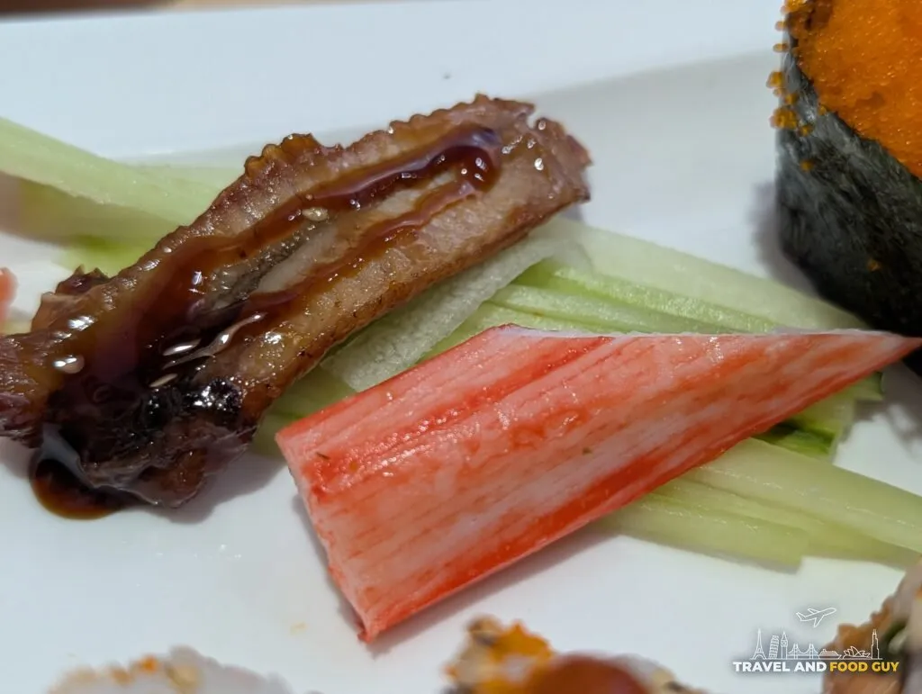 Glazed eel with sesame and a wedge of crab stick over julienned cucumber at e Sushi.
