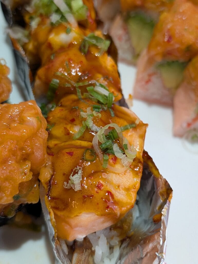 The baked Fire Dragon roll at e Sushi, salmon and white tuna over rice under a glossy baked spicy mayo, eel sauce and sliced green onion.