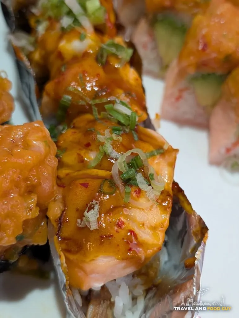 The baked Fire Dragon roll at e Sushi, salmon and white tuna over rice under a glossy baked spicy mayo, eel sauce and sliced green onion.