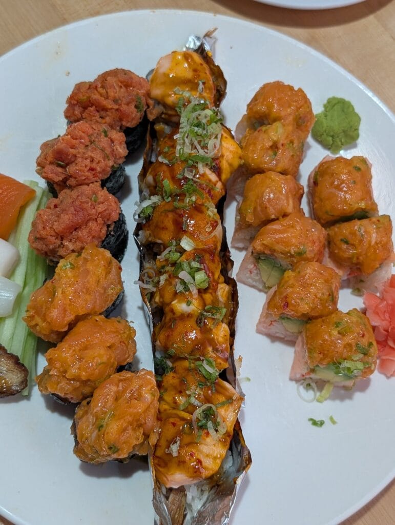 The first plate at e Sushi: spicy tuna and spicy salmon gunkan on the left, the baked Fire Dragon roll down the middle under eel sauce, spicy mayo and green onion, and the Sakura roll in pink soy paper on the right.
