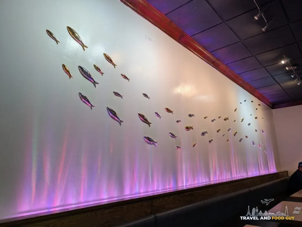 A shoal of polished metal fish running along the banquette wall at e Sushi, lit from below in shifting pink and violet.