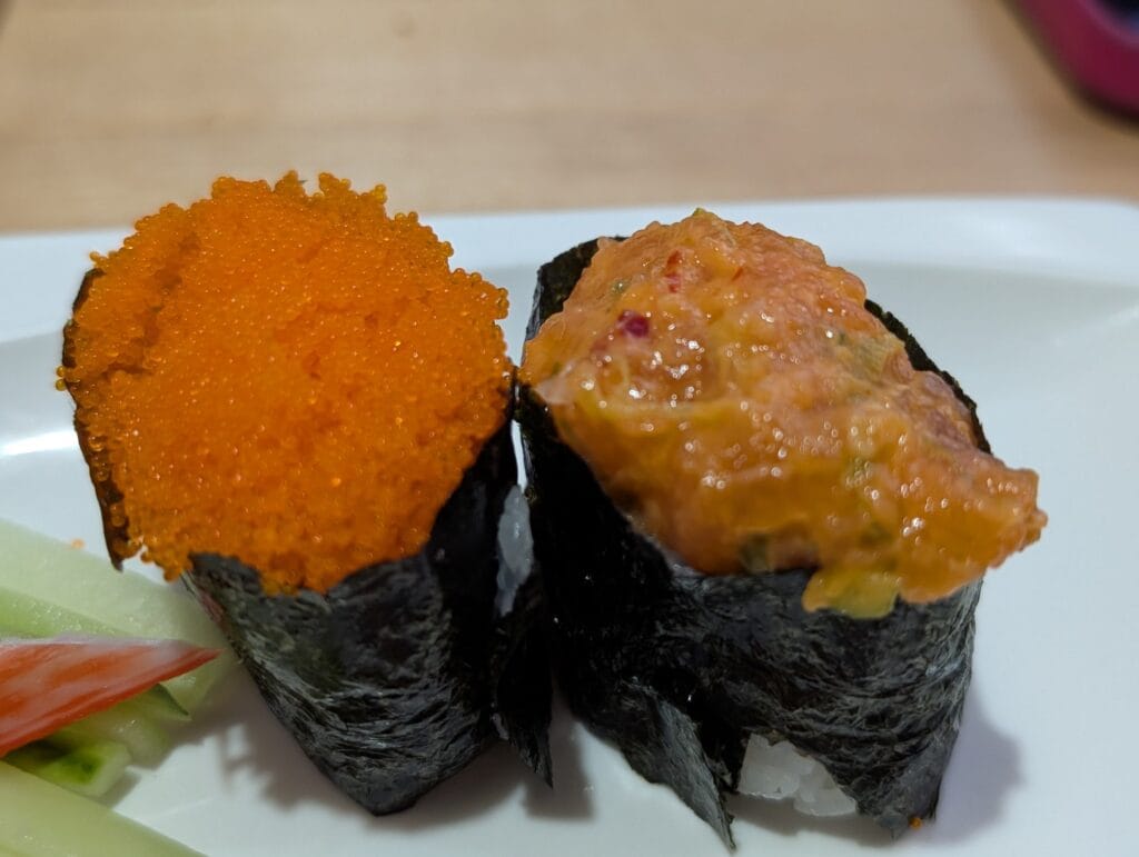 Two gunkan at e Sushi side by side, bright orange masago on the left and spicy salmon with scallion on the right.