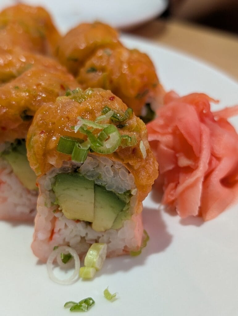 A cut end of the Sakura roll at e Sushi, crab and avocado inside, spicy salmon and scallion on top, with pickled ginger alongside.