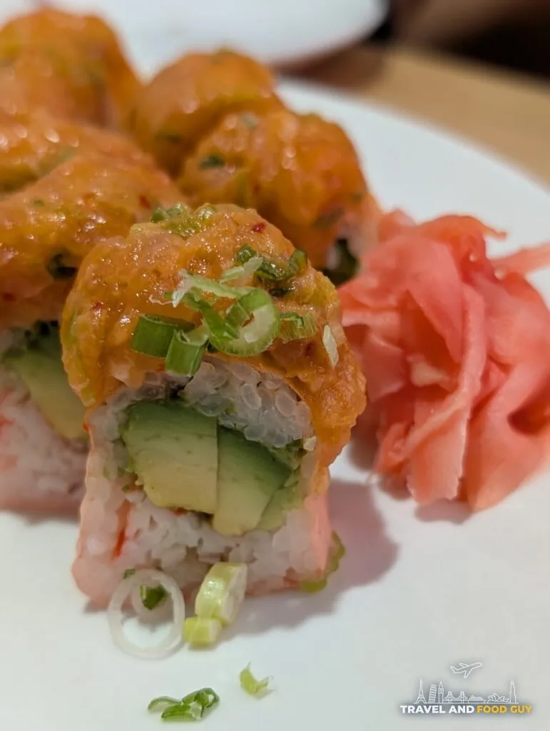 A cut end of the Sakura roll at e Sushi, crab and avocado inside, spicy salmon and scallion on top, with pickled ginger alongside.