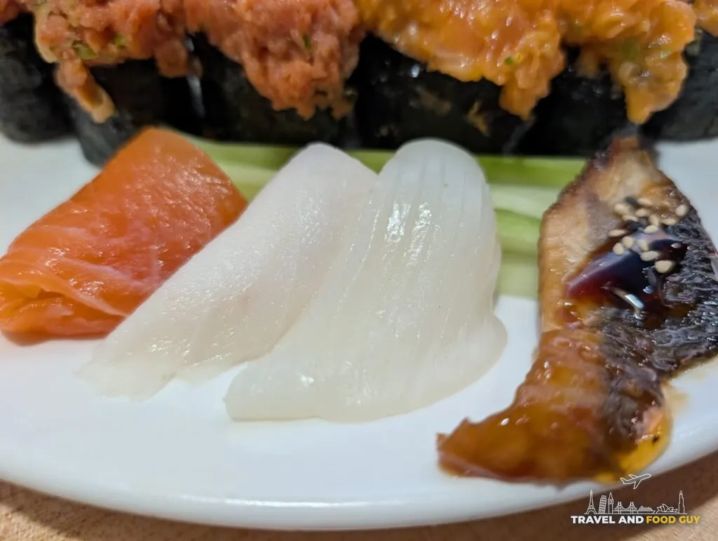 Side sashimi at e Sushi: salmon on the left with no visible marbling, two translucent slices of squid in the middle, and glazed eel with sesame on the right.