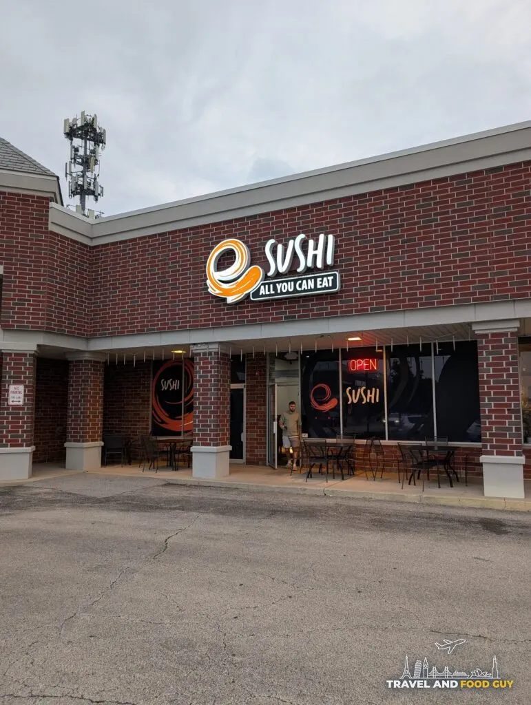 The entrance to e Sushi in Mount Prospect, with sidewalk tables and the neon OPEN sign in the window.