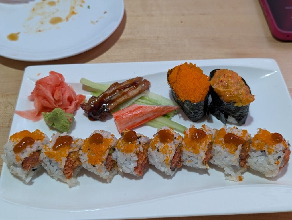 The Volcano roll at e Sushi, rice outside with spicy tuna in the middle, dusted with tobiko and sesame and dotted with chili sauce, plated with eel, crab stick and gunkan.