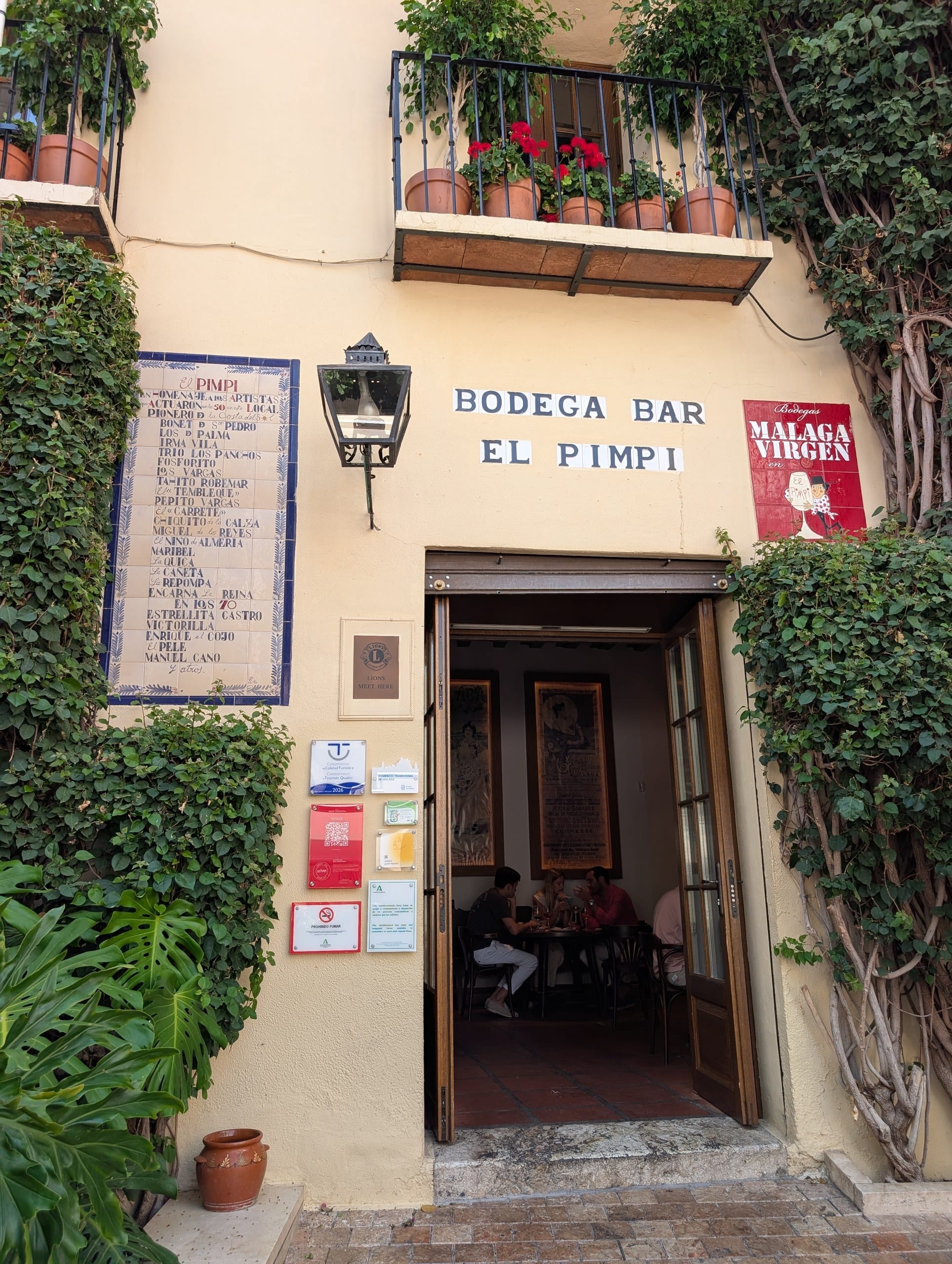 Bodega Bar El Pimpi doorway with a painted tile panel of performers and ivy on the walls