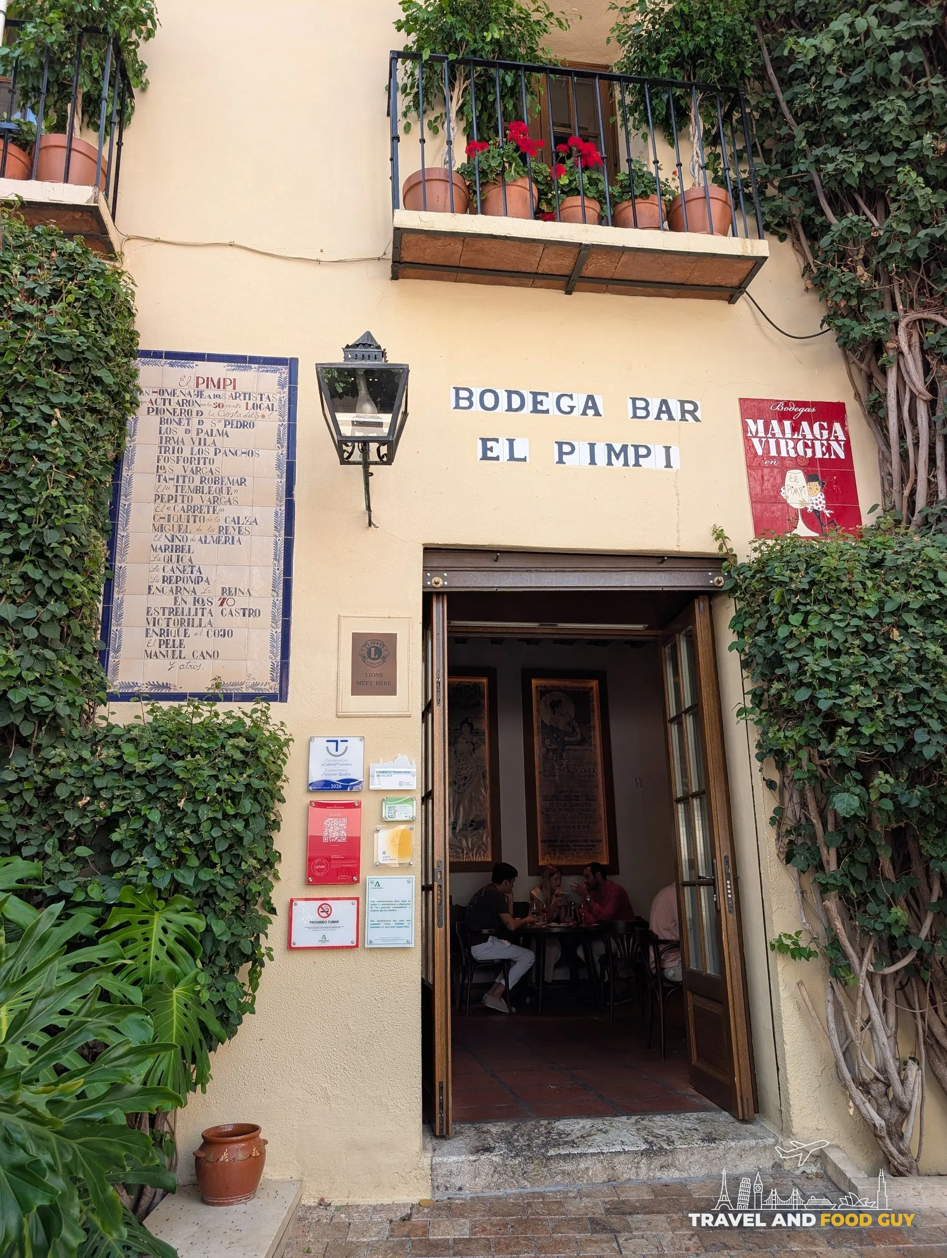 Bodega Bar El Pimpi doorway with a painted tile panel of performers and ivy on the walls